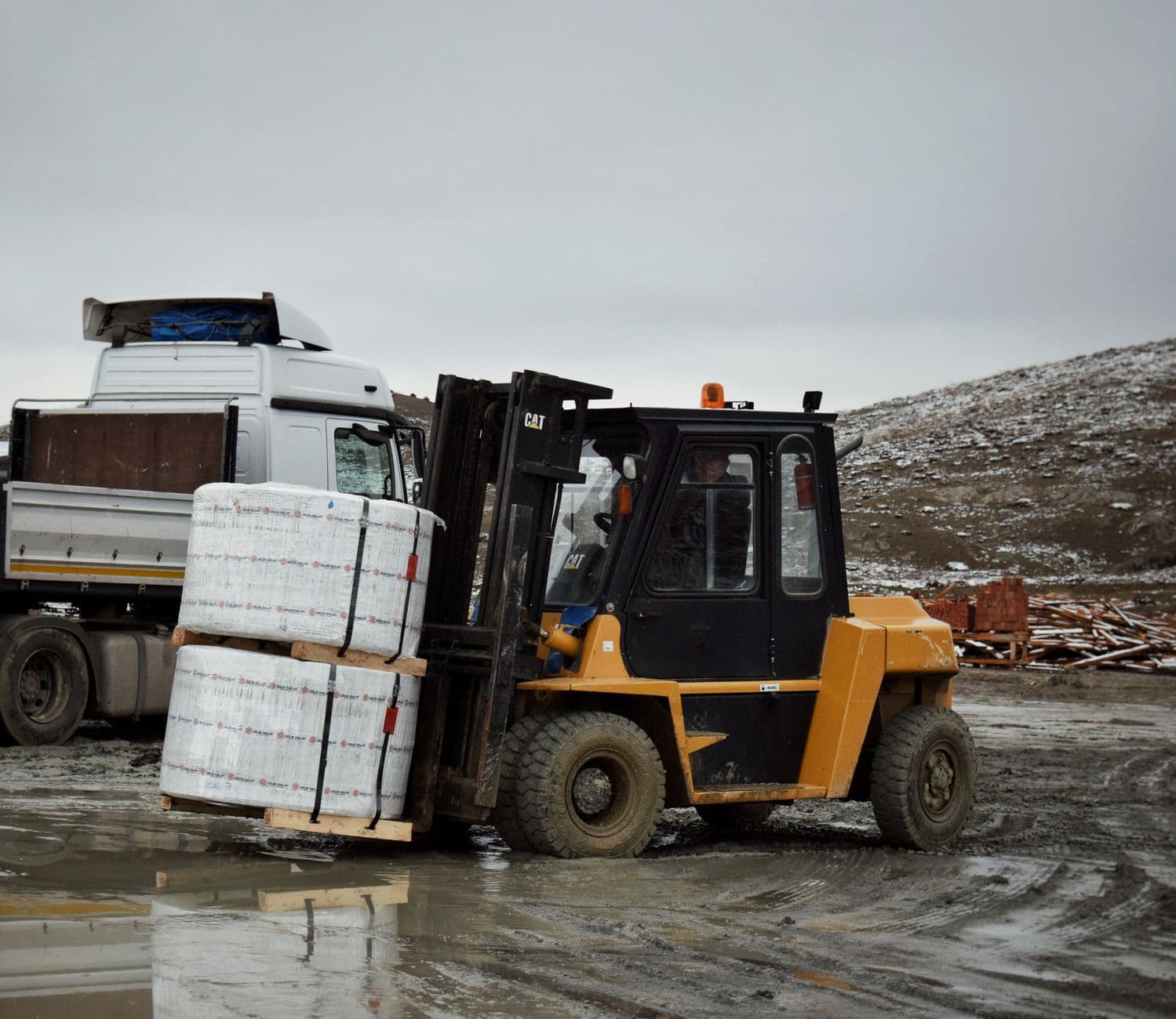 Forklift carrying stacked goods beside a truck
